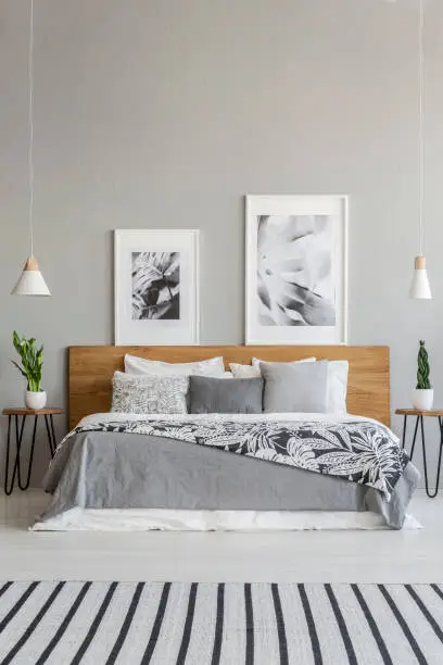 Posters on wooden headboard of bed with patterned blanket in grey bedroom interior with carpet. Real photo
