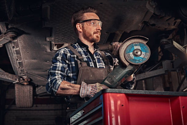 istock Mechanic in a uniform and safety glasses holds an angle grinder while standing under lifting car in a repair garage. 1019976422