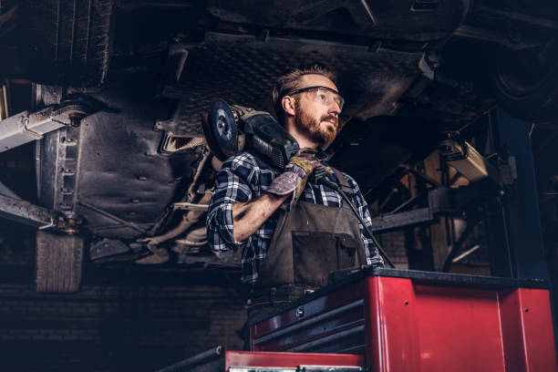 istock Mechanic in a uniform and safety glasses holds an angle grinder while standing under lifting car in a repair garage. 1019976896