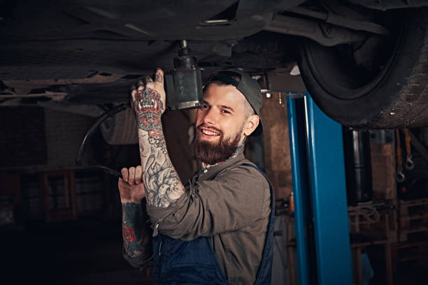istock Auto mechanic in a uniform, repair the car with a screwdriver while standing under lifting car in the repair garage. 1019981838