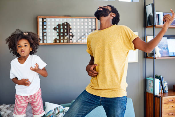 Time for an air guitar solo! Shot of a cheerful young father and his son dancing on a couch while listening to music at home during the day air guitar stock pictures, royalty-free photos & images