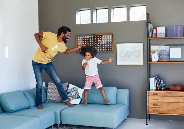 We are rockstars today! Shot of a cheerful young father and his son dancing on a couch while listening to music at home during the day air guitar stock pictures, royalty-free photos & images