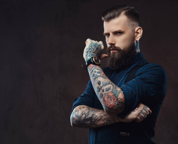 Pensive handsome old-fashioned hipster in a blue shirt and suspenders, standing with hand on chin in a studio. stock photo