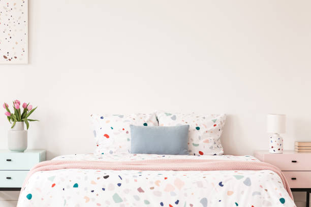 istock Real photo of a double bed with dotted sheets and pillows on an empty wall between nightstands in a bedroom interior. Place for your painting/poster/clock 1019992704