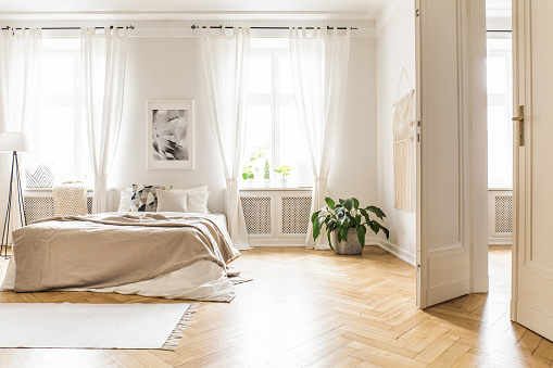 Spacious and bright bedroom interior with beige decorations, hardwood floor and a book on the window sill seat