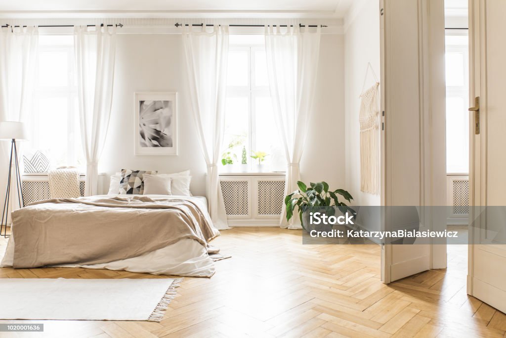 Spacious and bright bedroom interior with beige decorations, hardwood floor and a book on the window sill seat Bedroom Stock Photo