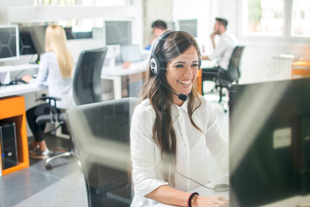 bela mulher sorridente com fones de ouvido usando o computador enquanto o aconselhamento para o call center - bluetooth headset women customer - fotografias e filmes do acervo