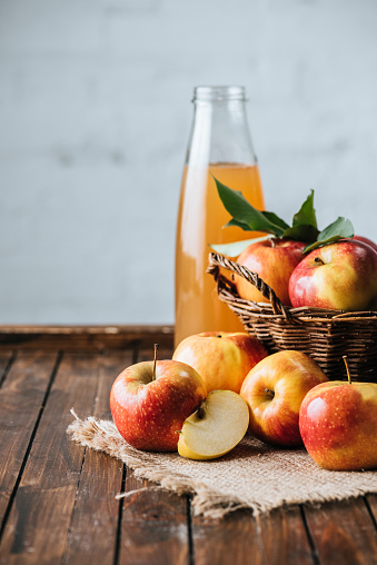 close up view of glass bottle of apple juice and apples in basket on wooden tabletop