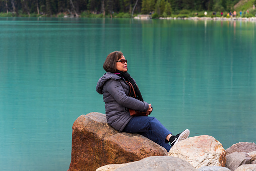 Lake Louise, Banff, Canada -- August 3, 2018.  A tourist sits on a rock posing for a photo at Lake Louise.