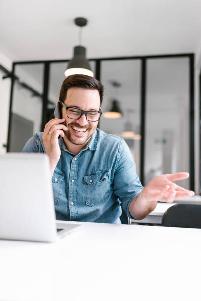 istock Smiling man talking on the phone at work indoors. 1020064744