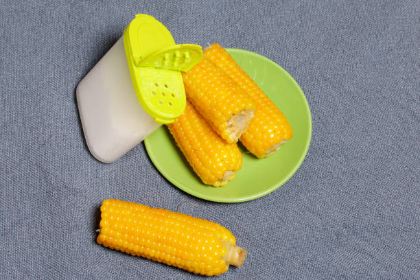 Cobs of boiled corn and salt in a salt shaker. Against the background of sacking.
