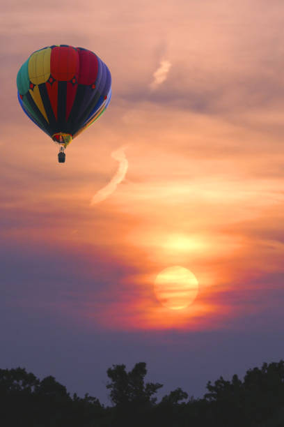 A hot air balloon flies against a beautiful sunset landscape.