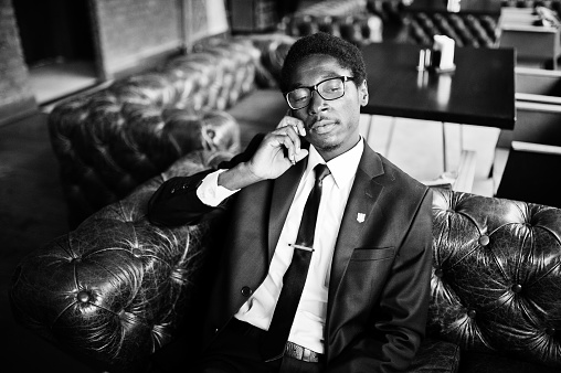 Business african american man wear on black suit and glasses sitting at office and speaking on phone.