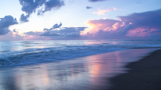A beautiful sunrise filled with shades of pink, magenta and blue. The colors of the sky reflected on the wet sand and smooth surface of the ocean. Long exposure gives a softness and sense of motion.