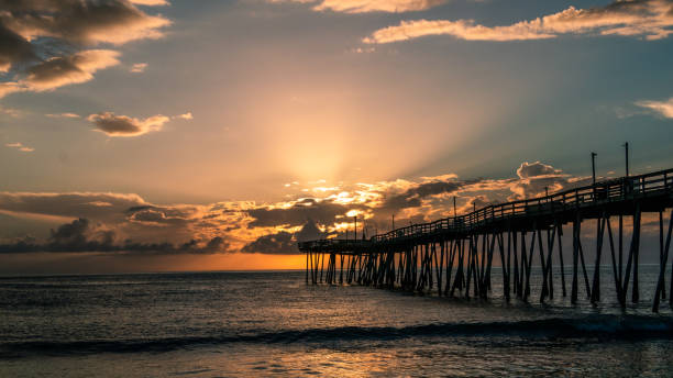 istock Light rays explode from the clouds at sunrise to light the sky and ocean pier. 1020118512