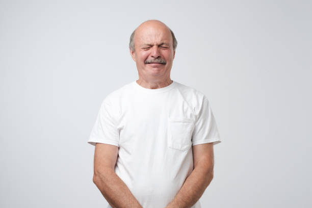 infeliz hombre senior como llorón llorando de pie sobre fondo gris. él es ofendido y molesto. - hacer muecas fotografías e imágenes de stock