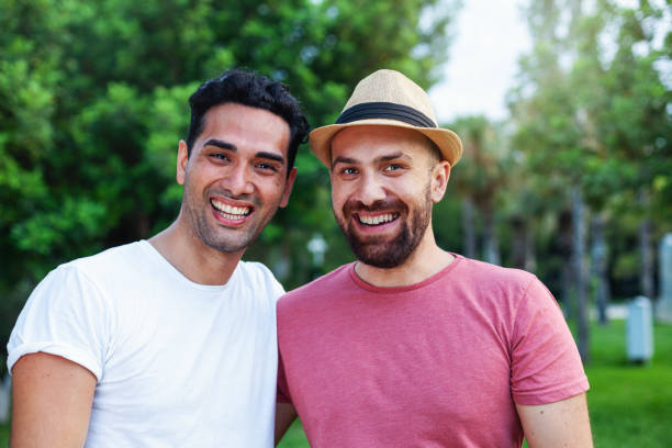 Multi ethnic gay couple hugging Two young man looking at the camera and smiling together in the park gay man photos stock pictures, royalty-free photos & images