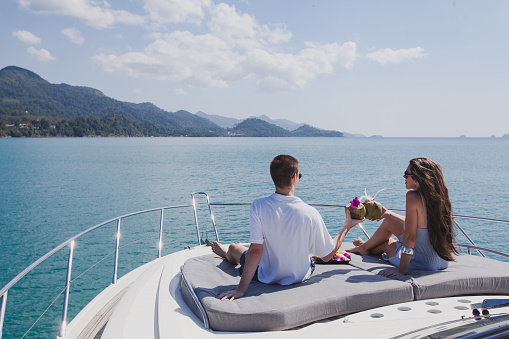 couple enjoying honeymoon onboard of luxury boat, luxurious yacht in tropical sea, man and woman drinking coconuts and relax
