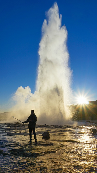 Male tourist took photo himself in between Geysir hot spring eruption.