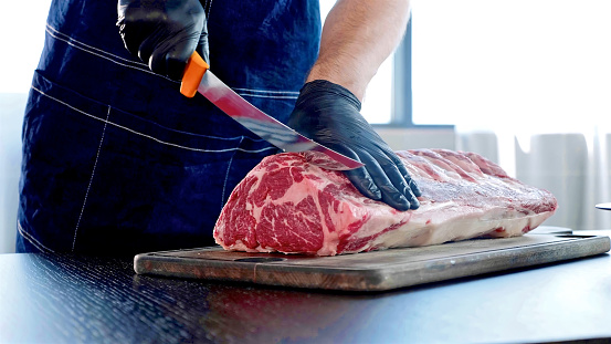 Chef cuts raw meat on the wood board with the knife, close-up. Chopping meat for cooking steak at reastaurant.