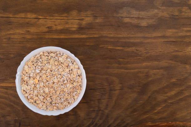 istock White bowl filled with oat flakes, top view on wooden background. 1020206064