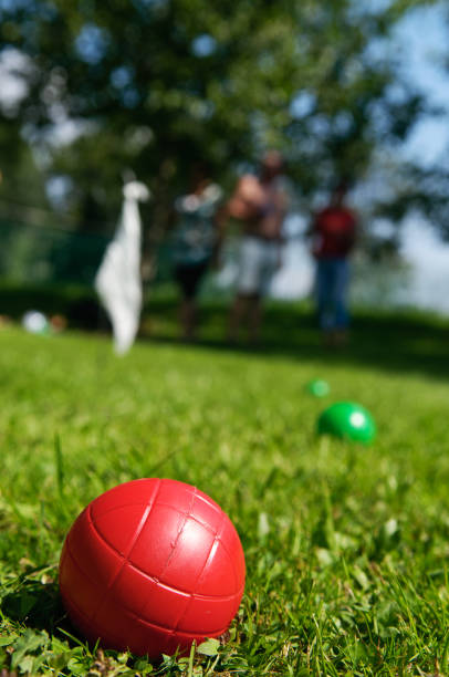 Closeup of red boccia ball lying in grass and people playing in background stock photo
