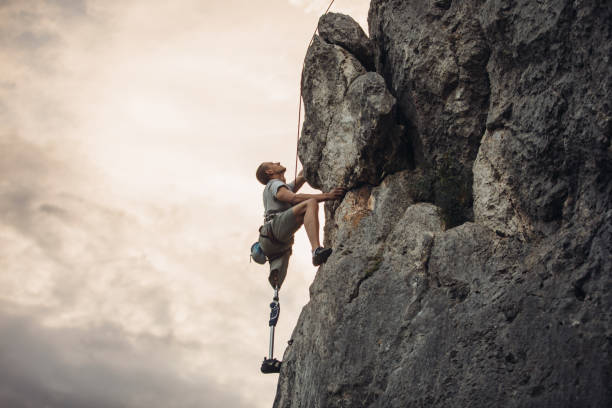 Disability man climber One man, disability young man with prosthetic leg free climbing on a rock in nature.. disabled person hiking outdoors stock pictures, royalty-free photos & images