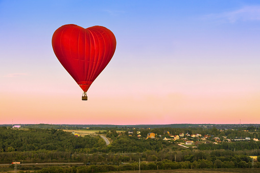 Heart Flying Red Hot Air Balloon in sunset sky under green grass.