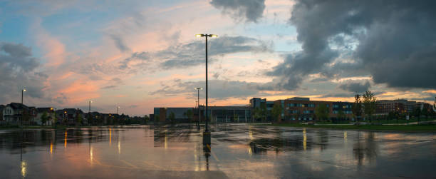Lamps illuminate this view of a parking lot at dusk