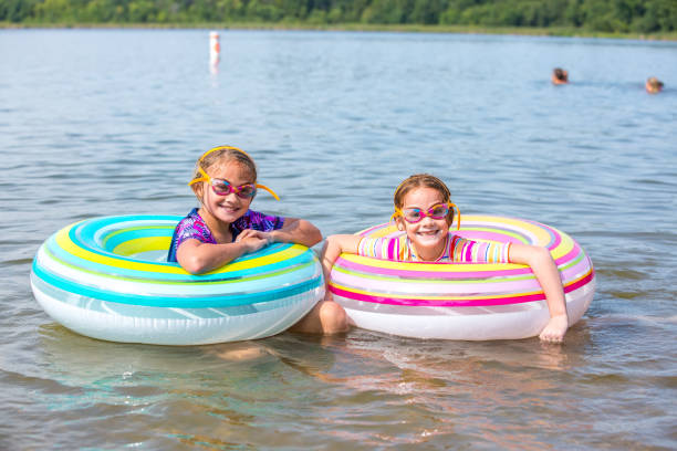 две девушки в innertube плавать игрушки на пляже - inner tube swimming lake water стоковые фото и изображения