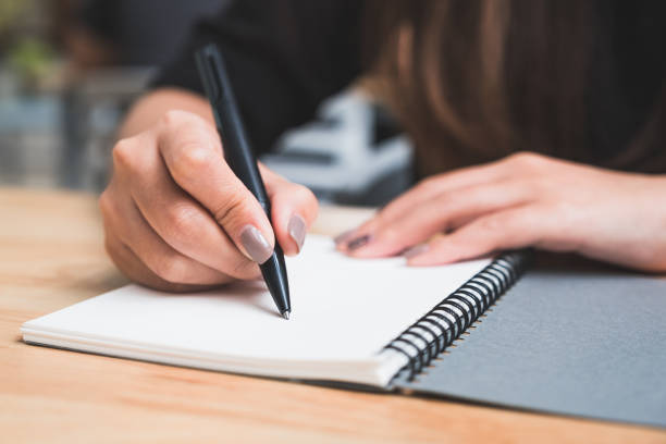 istock Closeup image of a woman writing down on a white blank notebook on wooden table 1020325328