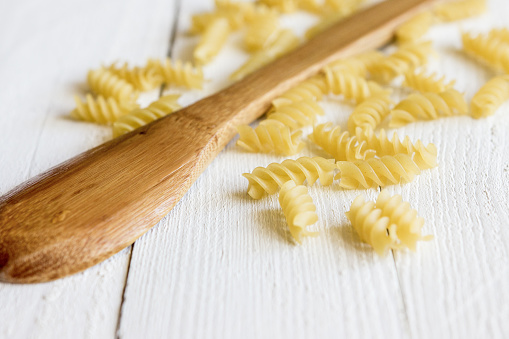Italian pasta near a wooden spoon on a white wooden table