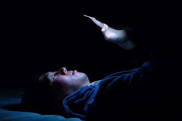 istock Asian young man using phone in dark bedroom with blue light phone screen - unhealthy eyes strain concept. 1020375596