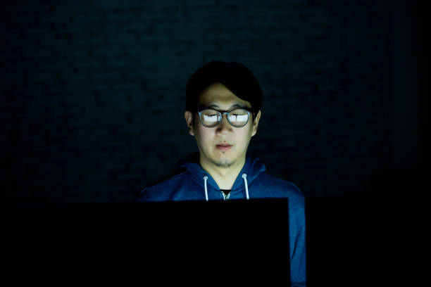 giovane asiatico che usa il computer nella stanza buia - concetto di occhi malsani. - looking at camera glasses serious men foto e immagini stock