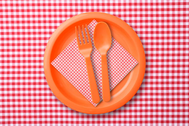 Overhead shot of orange plastic plate with folk and spoon on red gingham check tablecloth.