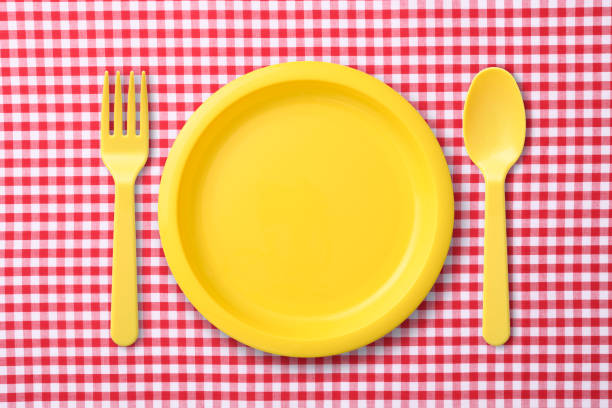 Overhead shot of yellow plastic plate with folk and spoon on red gingham check tablecloth.