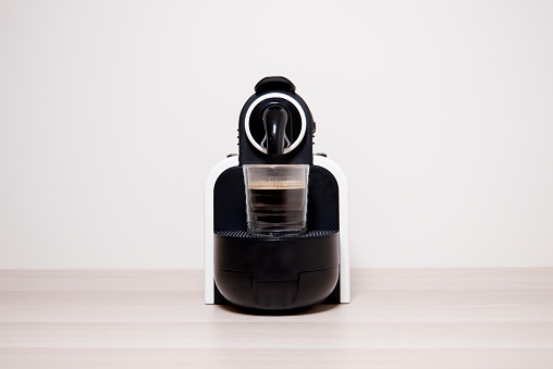 Coffee espresso capsule machine maker and glass against plain neutral background uk