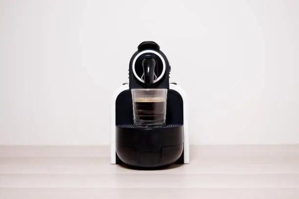 Coffee espresso capsule machine maker and glass against plain neutral background uk