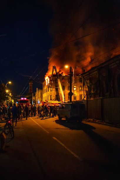 Night fire in apartment building, firefighters struggle with flame, silhouettes of unrecognizable people stand around. Fire disaster and accident tragedy concept, toned