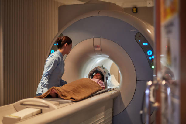 Nurse Looking At Girl During Cat Scan Exam Nurse looking at little patient in preparing for CAT scan. Girl with female healthcare worker during tomography exam. They are at hospital. mri scanner stock pictures, royalty-free photos & images
