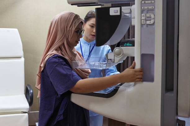 Nurse Assisting Patient During Mammography Exam Nurse examining patient with medical equipment. Female healthcare worker is assisting woman during mammogram test. They are standing at hospital. cancer screening stock pictures, royalty-free photos & images