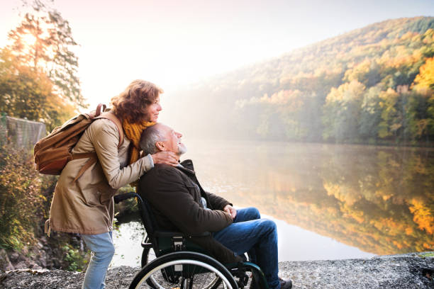 Senior couple with wheelchair in autumn nature. Active senior couple on a walk in a beautiful autumn nature. A woman and man in a wheelchair by the lake in the early morning. racewalking photos stock pictures, royalty-free photos & images