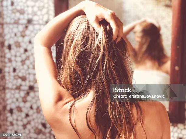 Beautiful Woman Touching Wet Hair While Looking In The Mirror In Bathroom Stock Photo - Download Image Now