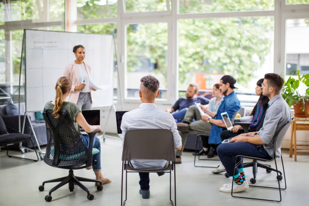 Multi-ethnic business people attending meeting Multi-ethnic business people attending meeting. Young businesswoman giving presentation to team at new office. organised group stock pictures, royalty-free photos & images