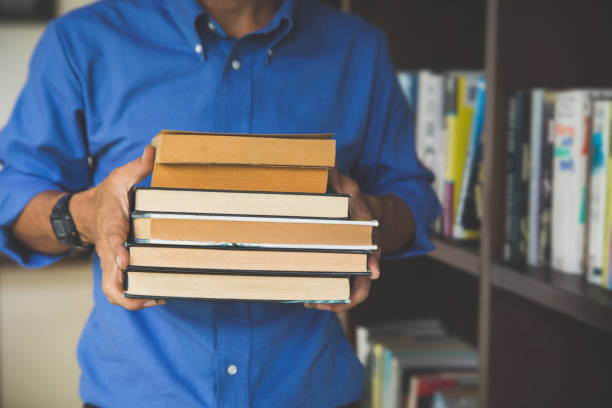 istock Man in a library holding books after doing a search and after studying. Concept: educational, portrait, library, and studious. 1020489604