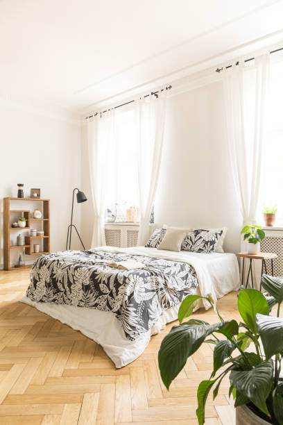 istock High ceiling bedroom interior with a comfortable bed with leaf pattern linen, a lamp and a bookcase. Real photo. 1020500920