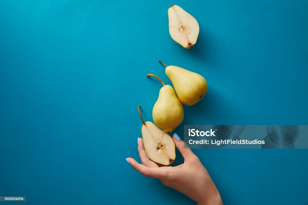 cropped image of woman taking half of pear from blue surface Adult Stock Photo