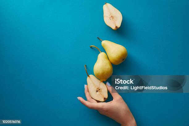 Cropped Image Of Woman Taking Half Of Pear From Blue Surface Stock Photo - Download Image Now