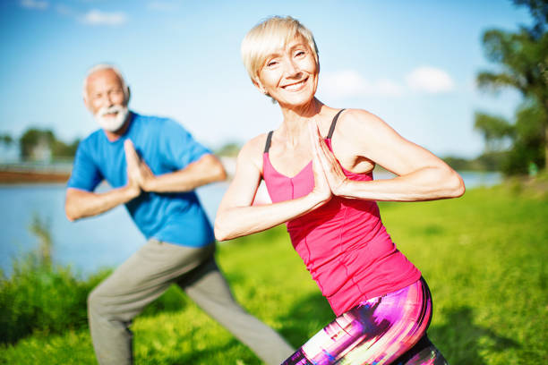 Senior Yoga. Senior couple doing standing prayer yoga pose with a twist. Looking at camera. Front view. Horizontal. twist pose stock pictures, royalty-free photos & images