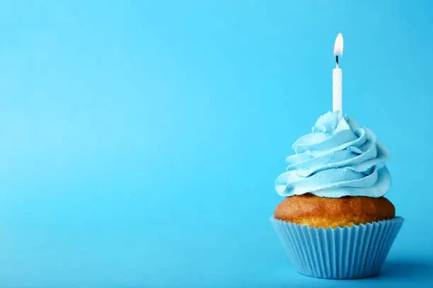 Tasty cupcake with candle on blue background